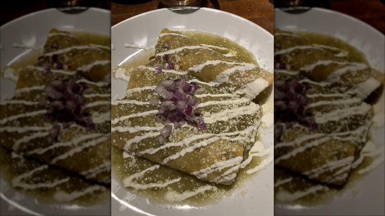 Three enchiladas verde on a white plate drizzled with sour cream and queso fresca and garnished with chopped red onion