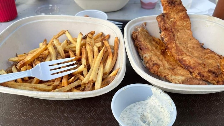 takeout containers with fried fish on one side and fries on the other with plastic ramekin of tartar sauce