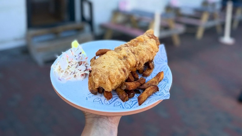 A blue plate with large piece of fried fish on fries with cole slaw