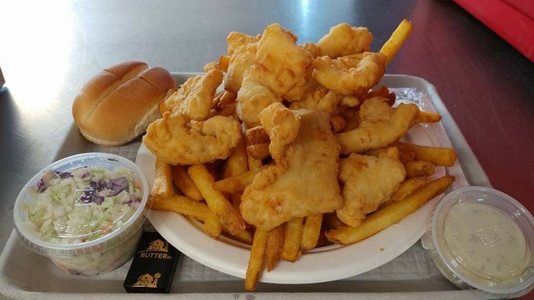 pile of fried fish and french fries with bread roll, coleslaw, and tartar sauce on side