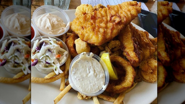 fried fish on top of fries served with lemon wedge, sauce, and cole slaw