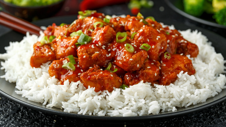Plate of General Tso's Chicken on bed of rice topped with sesame seeds and green onion