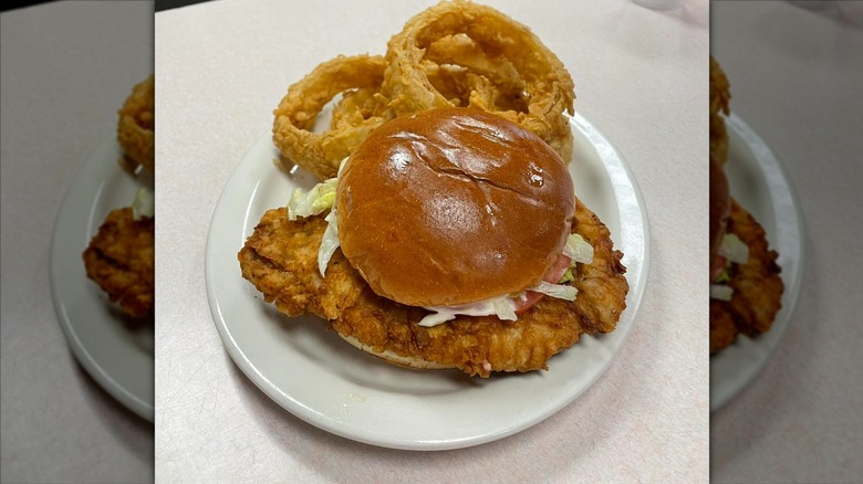 pork tenderloin sandwich with bun and onion rings on side