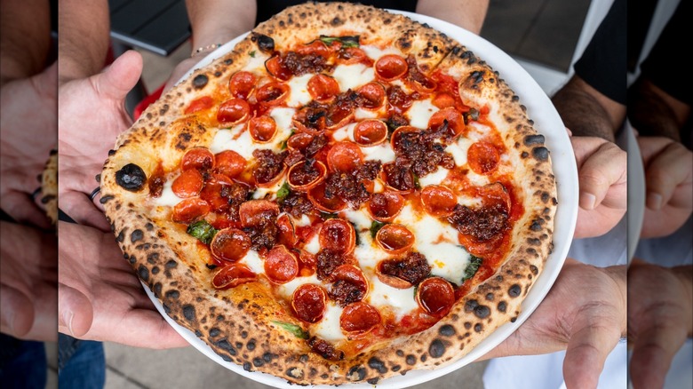 Three people holding up a plate of Cane Rosso pepperoni pizza