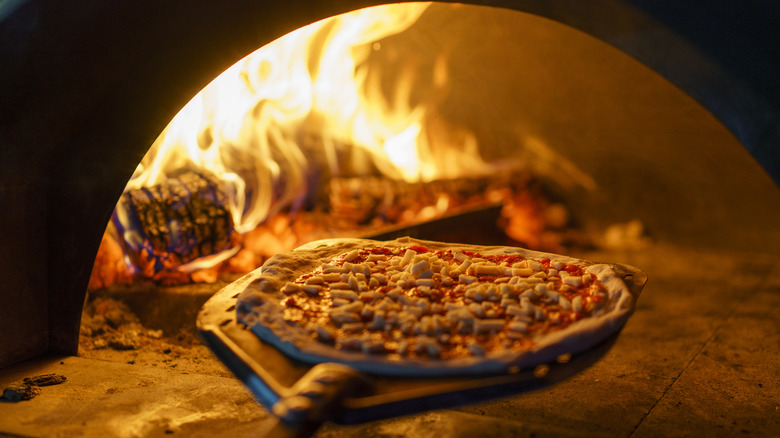 An uncooked pizza going into a wood-fired oven