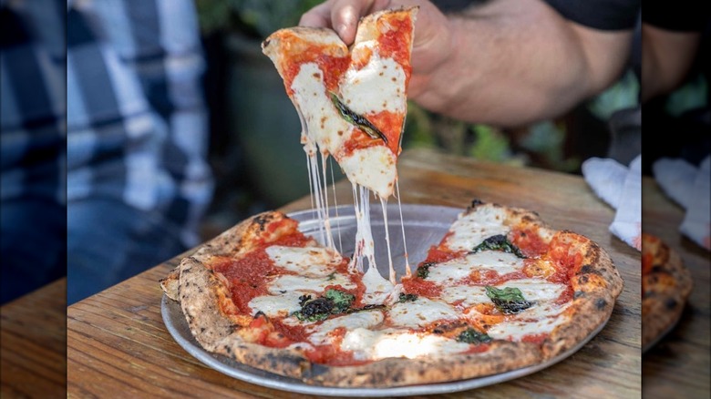 A person grabbing a slice of Oak & Rye Margherita pizza with a great cheese pull