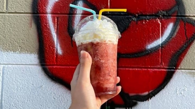 Milkshake with two straws and whipped cream, in front of a spraypainted mural.