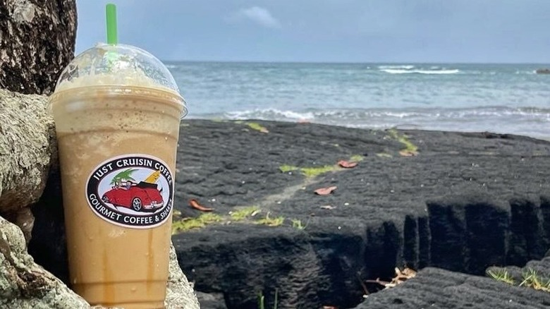Just Cruisin blended frozen beverage in plastic cup with green straw, on a Hawaiian beach.