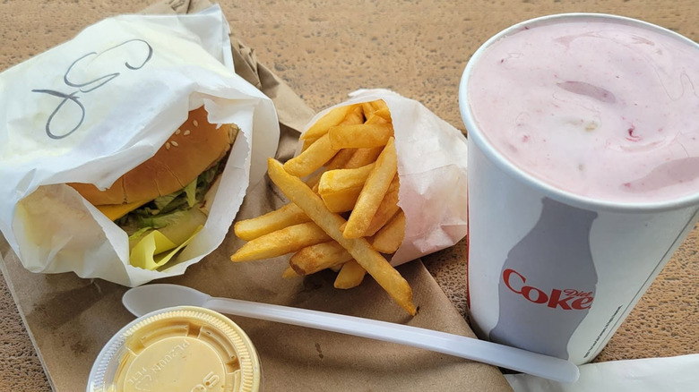 Burger, fries, and strawberry milkshake on a tray.