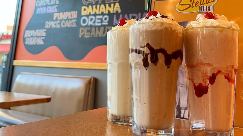 Milkshake trio in glasses topped with whiped cream, syrup and cherries, on a table in Stella's.