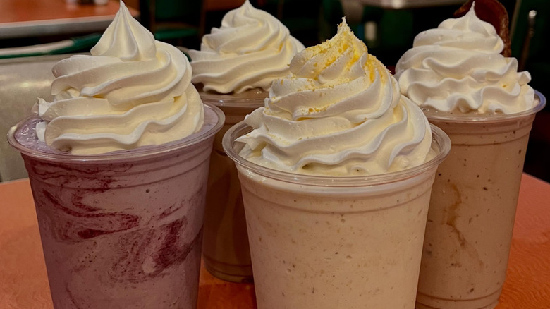 Four milkshakes, in plastic cups topped with whipped cream.
