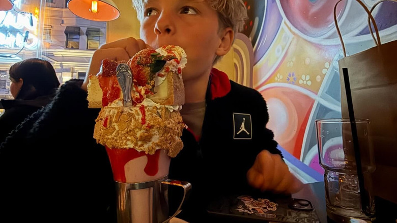 Boy drinking huge milkshake topped with cheesecake slice.
