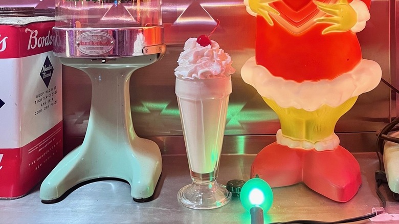 Milkshake with whip cream and cherry in glass, next to light-up Grinch and vintage-style blender.