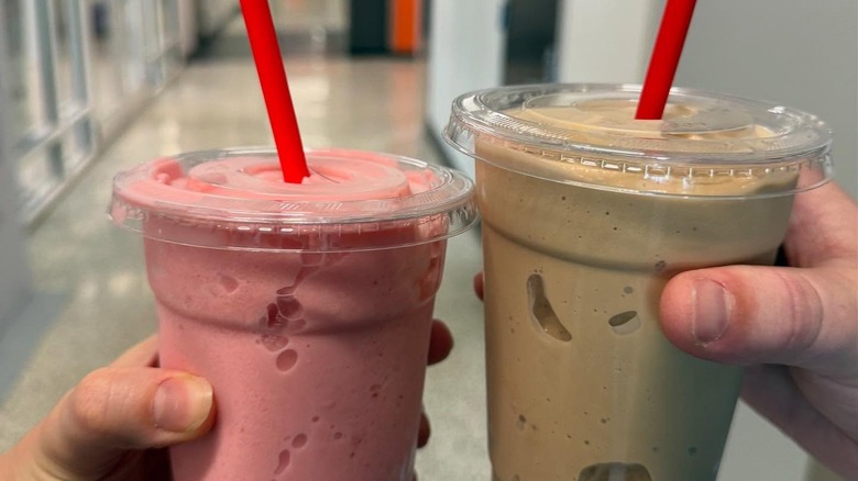 One pink and one chocolate milkshake in plastic cups with red straws.