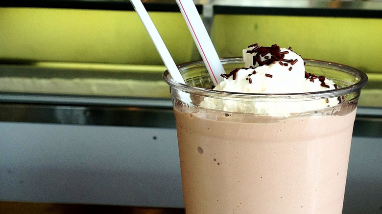 Chocolate milkshake in plastic cup with whipped cream and chocolate sprinkles.