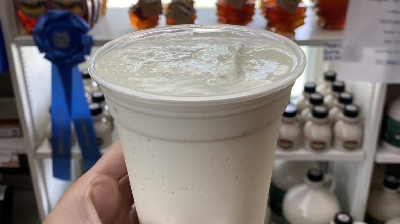 Maple milkshake in plastic cup, with maple syrup and blue ribbon in background.