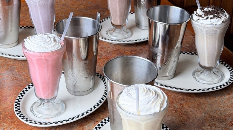 Variety of milkshakes in glasses with mixing cups, on plates.