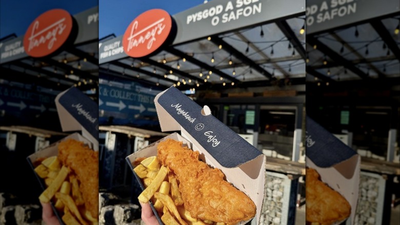 hnad holding box of fish and chips outside Finney's Benllech, Benllech, Anglesey