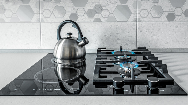 Kettle on induction stovetop next to two lit gas burners.