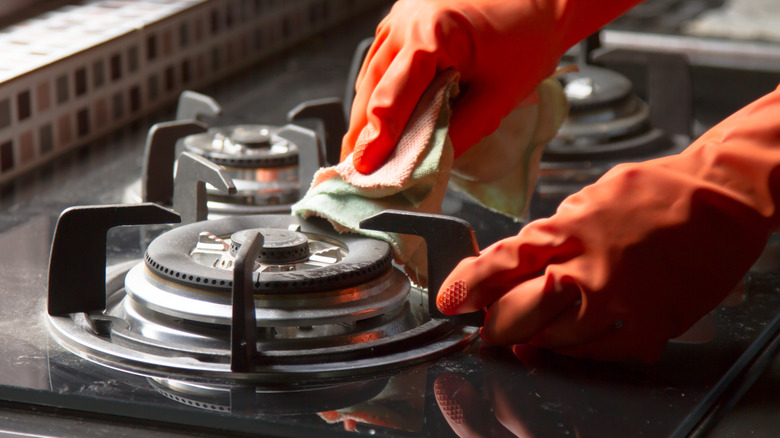 Gloved hands cleaning gas stove.