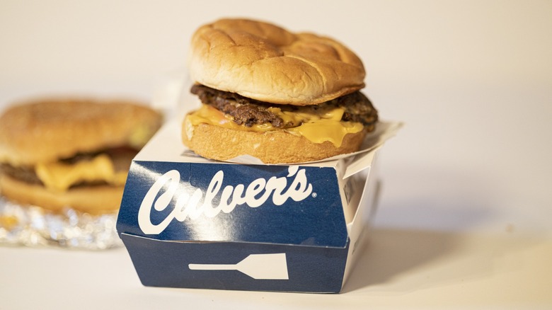 A Culver's ButterBurger with cheese displayed atop its box, with a Five Guys cheeseburger behind it.