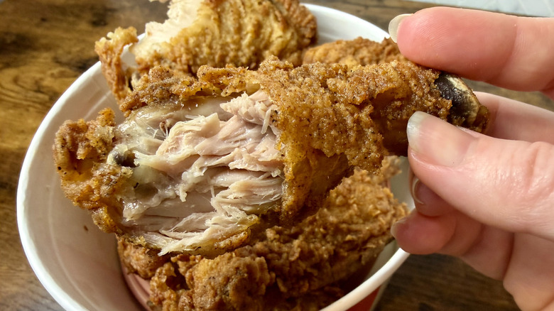 Hand holding a piece of KFC's Original Recipe fried chicken with a bite taken out