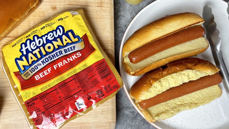 A package of Hebrew National 100% Kosher Beef Franks with two hot dogs beside it.