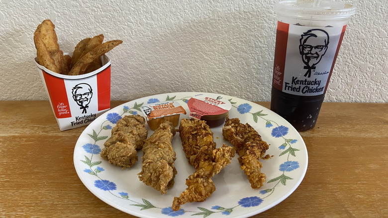 KFC tenders on plate with sauces beside potato wedges and drink