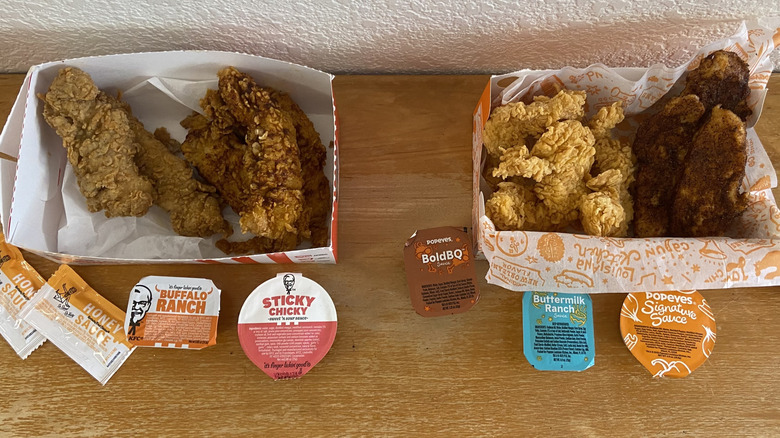 A top-down view of KFC and Popeyes tenders in boxes beside sauces