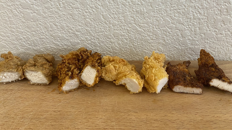 Halved cross-sections of each kind of KFC and Popeyes tender lined up on a table
