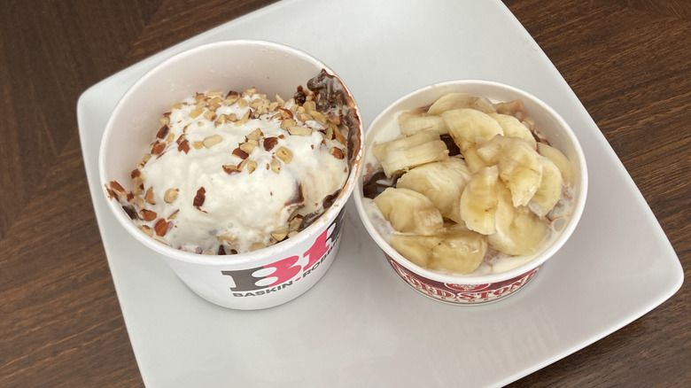 Baskin-Robbins sundae with chopped nuts and Cold Stone sundae with sliced bananas in paper cups