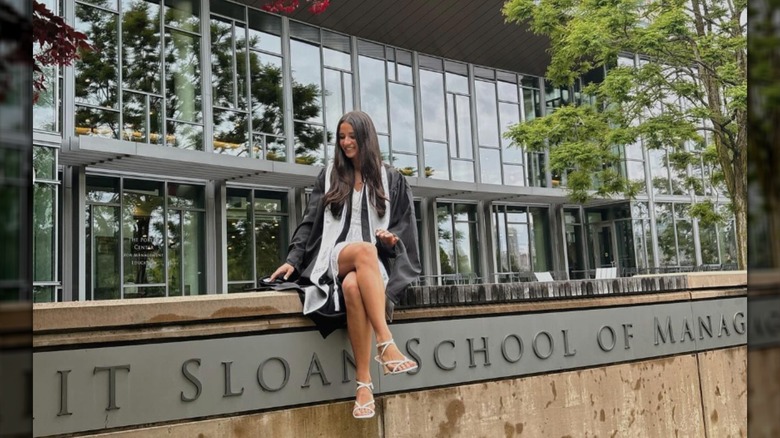 Isabelle Tashima wears her graduation toga and cap, and poses in front of the MIT Sloan School of Management campus signage
