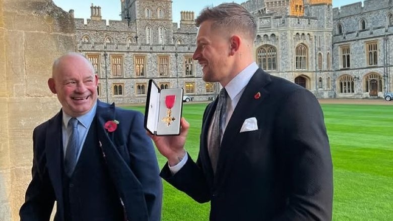 Adam Ramsay-Peaty holding his OBE medal after the ceremony with another attendee