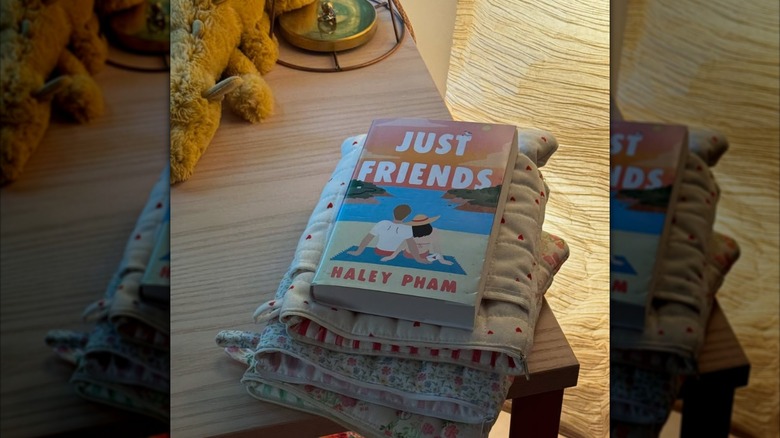 Copy of Just Friends by Haley Pham resting on a stack of book sleeves