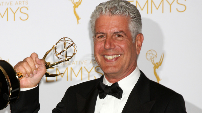 Anthony Bourdain smiling big and holding an Emmy award.