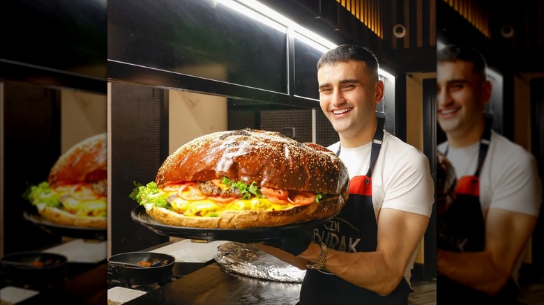 CZN Burak, also known as Burak Ozdemir, smiles brightly while holding up a giant burger