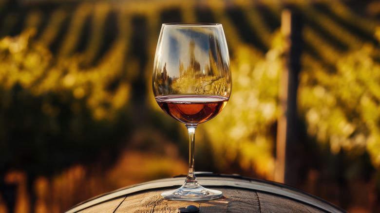 Glass of red wine on barrel outside.