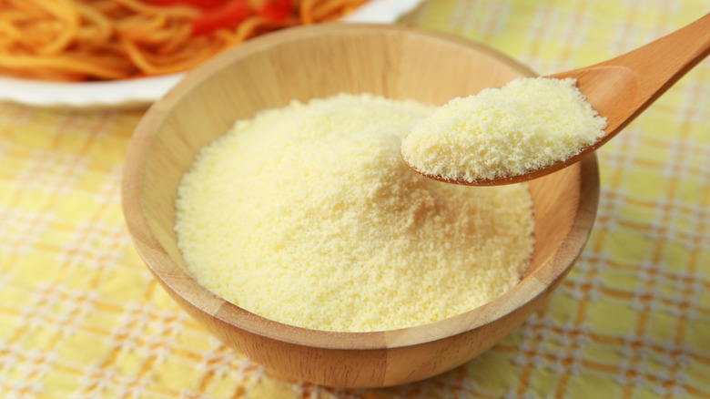 Wooden bowl of powdered parmesan cheese with spoon.