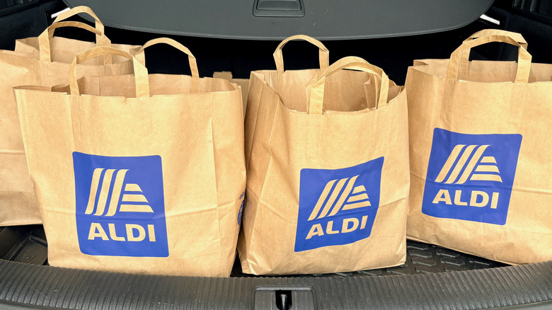 Multiple brown paper shopping bags with blue Aldi logos in the trunk of a car