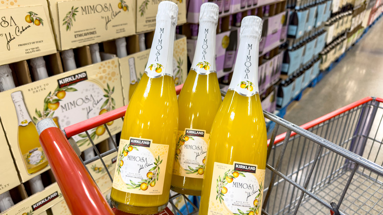 Three bottles of the Kirkland Signature mimosa in a shopping cart at a Costco warehouse store.