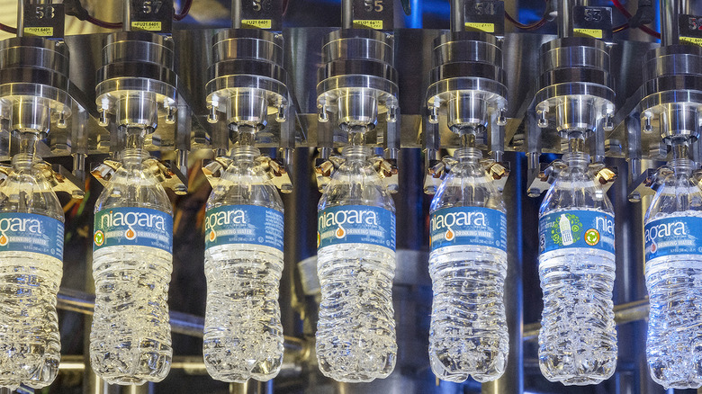Clear plastic bottles of water with blue Niagara labels are filled by a metal assembly line