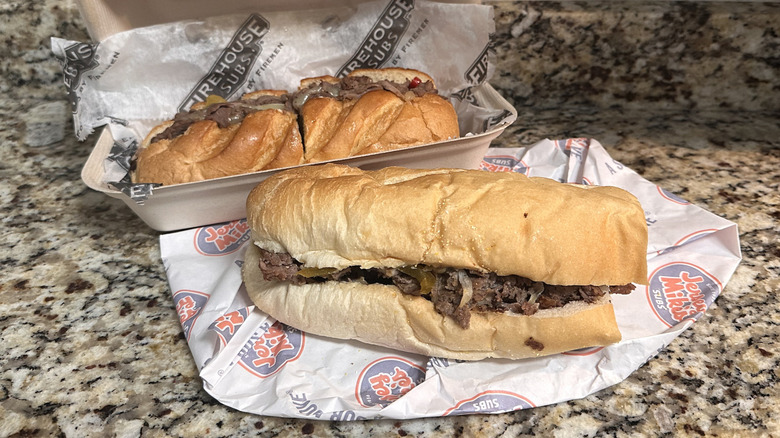 Firehouse and Jersey Mike's cheesesteak subs in their wrappers on counter.