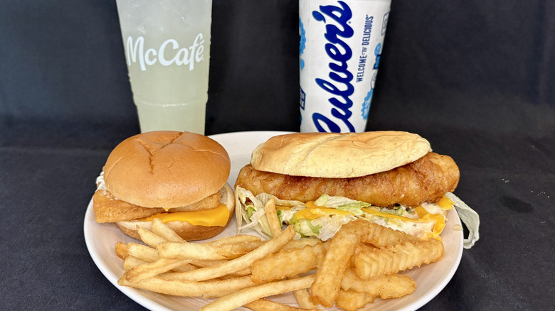 Two fish sandwiches on a white plate with french fries and McCafe and Culver's drink cups behind them