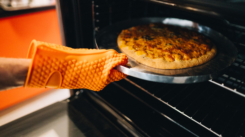 Person wearing an safety mitt to remove pizza from oven.