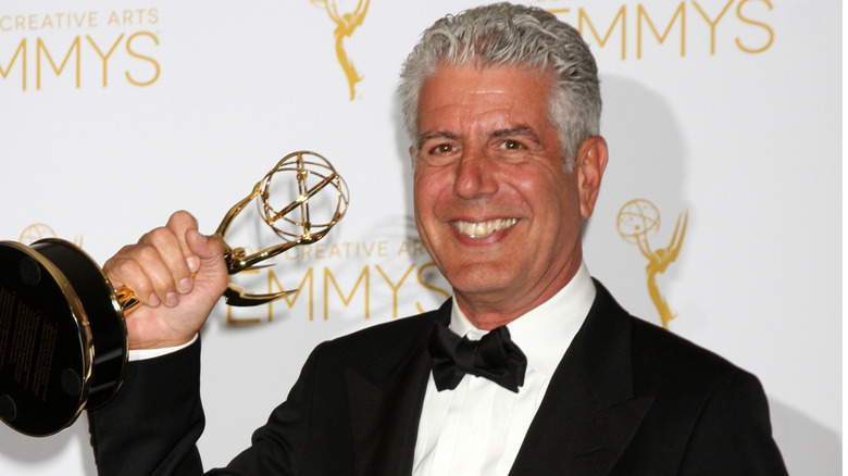 Anthony Bourdain smiling big and holding an Emmy award.