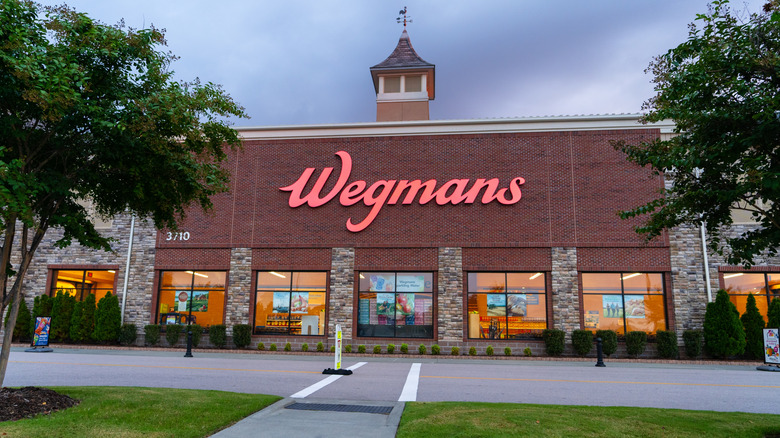 Exterior of a Wegmans supermarket at dusk with trees and a brick wall facade
