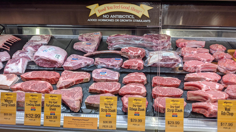 Multiple beef steaks on a black surface inside a display case in a Wegmans supermarket