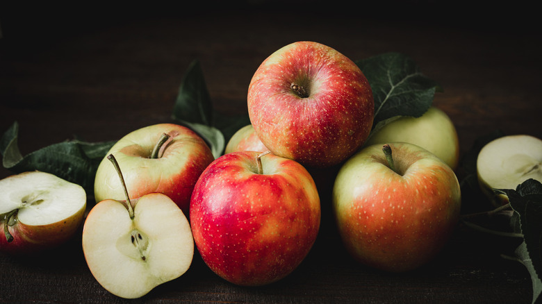 Red and green apples, some sliced, against dim backlighting