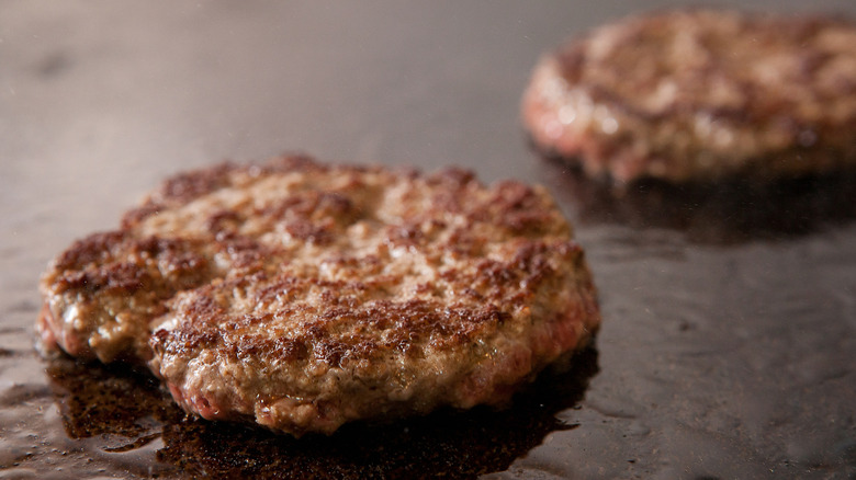 Close-up of two burger patties cooking on a griddle