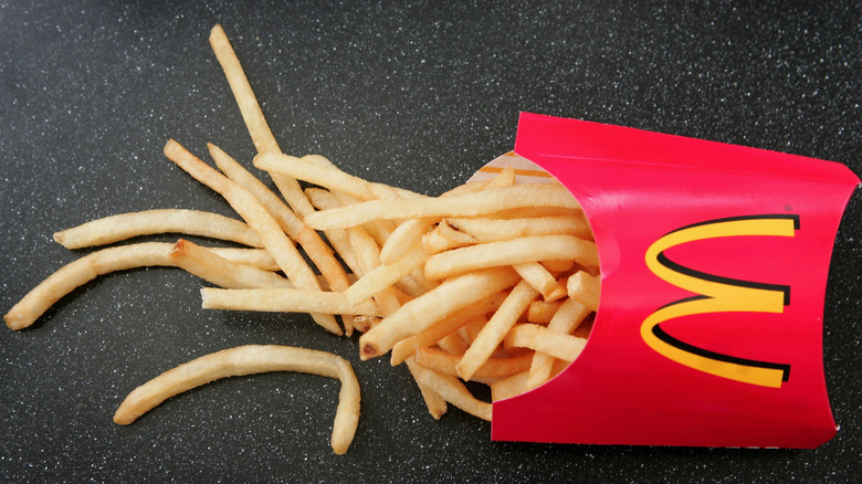 Top view of a McDonald's french fries container and thin-cut fries spilling over a dark tabletop